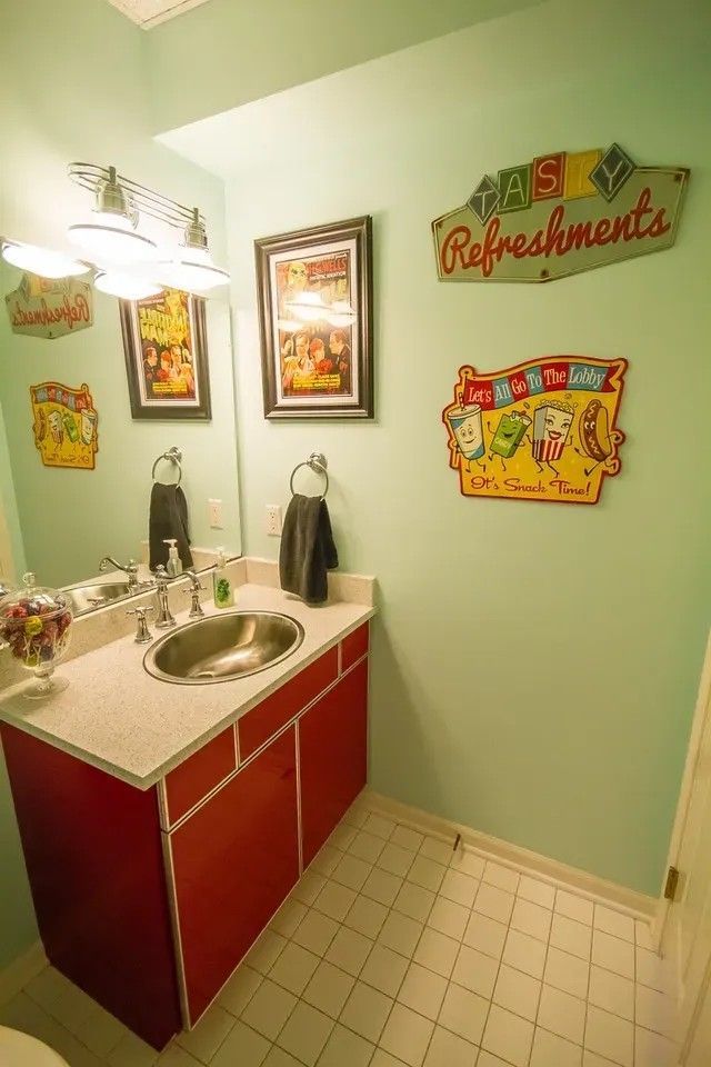 A bathroom with mint green walls, a red vanity cabinet, a silver sink, and retro-style diner wall art.