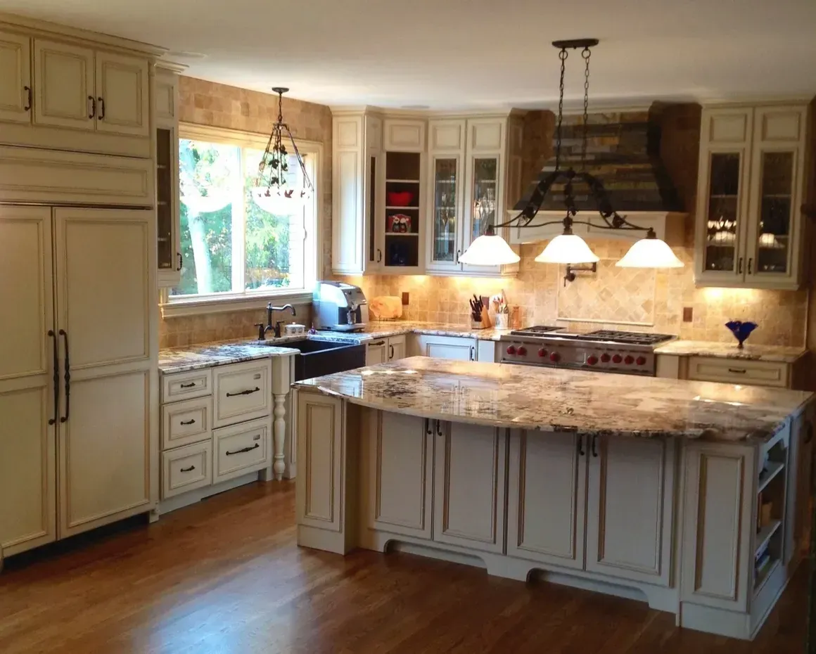 A cream-colored kitchen with a large granite island, stainless steel appliances, and a rustic vent hood above the stove.