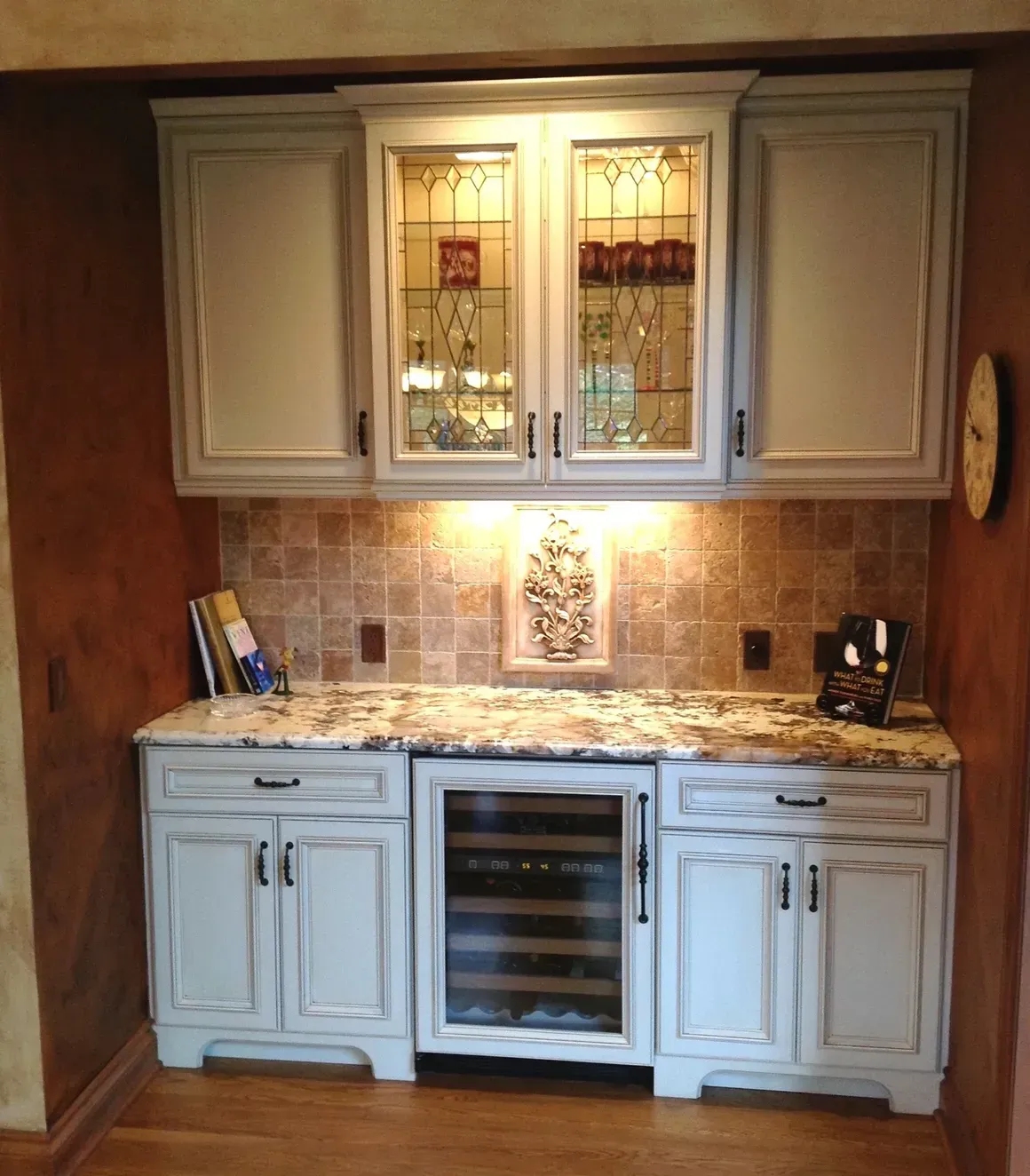 A kitchen wet bar with cream cabinets, granite countertops, a built-in wine cooler, and a tiled backsplash.
