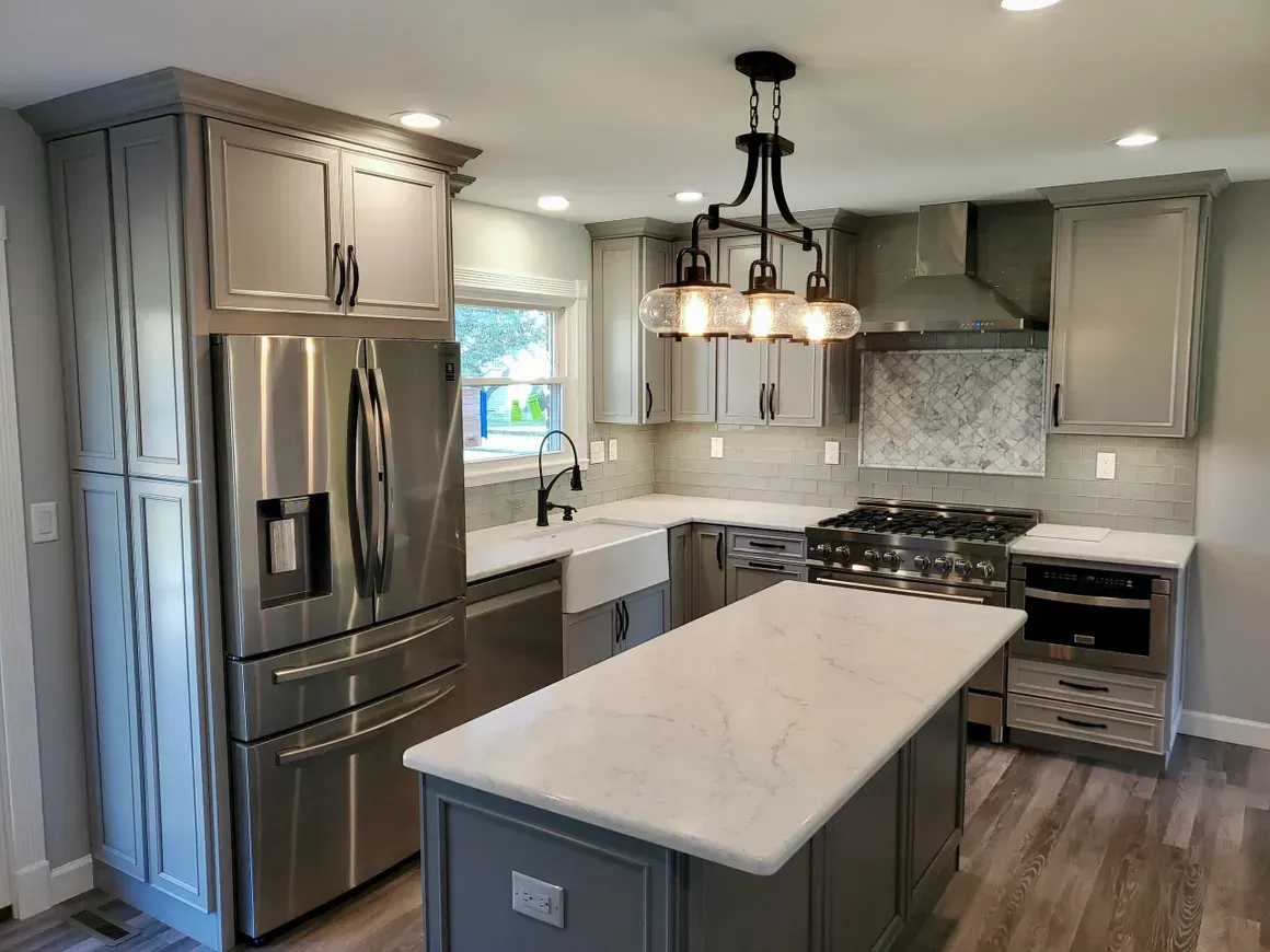 Modern kitchen with gray cabinets, white marble countertops, a central island, stainless appliances, and a glass chandelier.