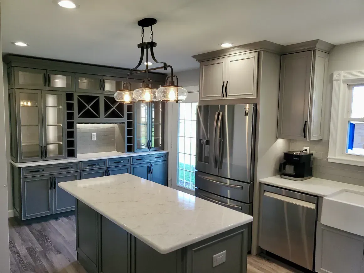 A modern kitchen featuring grey cabinets, a white marble island with a chandelier, and stainless steel appliances.