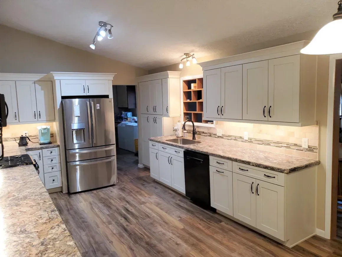 A well-lit kitchen with cream-colored cabinets, granite countertops, stainless steel refrigerator, and wood-look flooring.