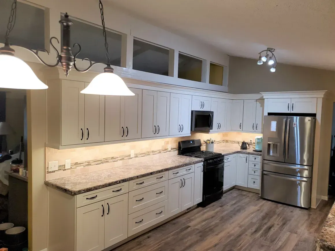 A kitchen with white cabinets, granite countertops, stainless steel appliances, and transom windows above the upper cabinets.