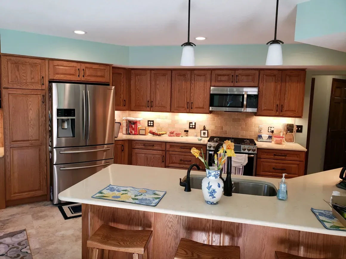 A kitchen with oak cabinets, stainless steel appliances, a center island with a vase, and light blue walls.