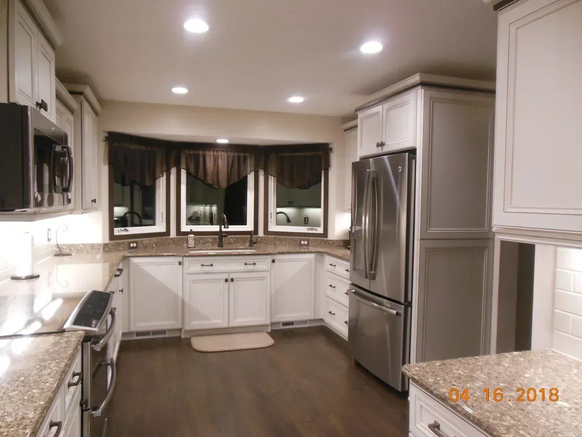 A modern kitchen featuring white cabinets, stainless steel appliances, granite countertops, and a bay window.