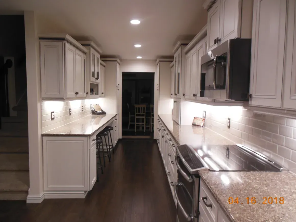 Galley kitchen with white cabinets, granite countertops, under-cabinet lighting, and dark hardwood floors.
