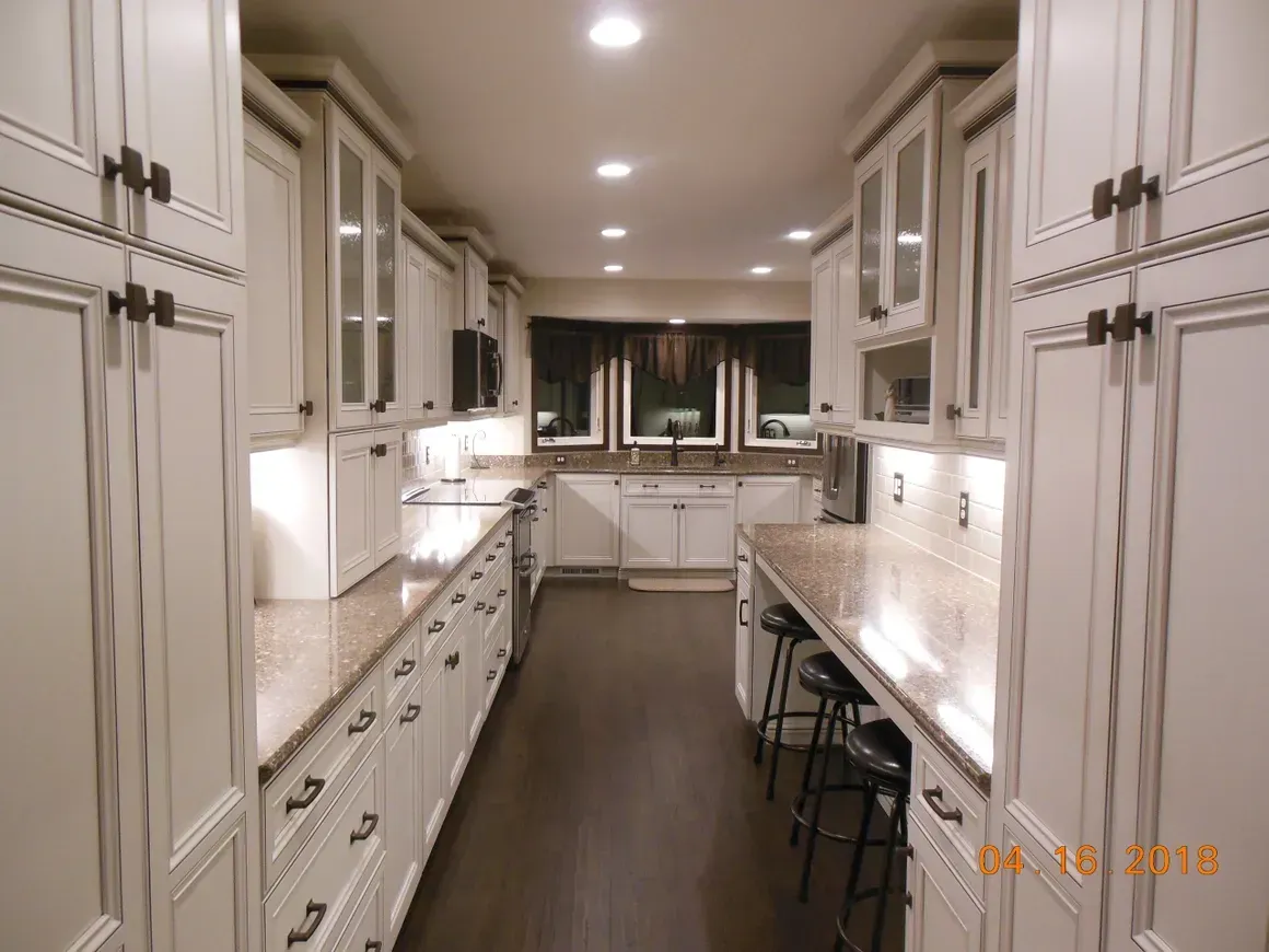 Galley kitchen with cream-colored cabinetry, marble countertops, dark wood floors, and recessed lighting.