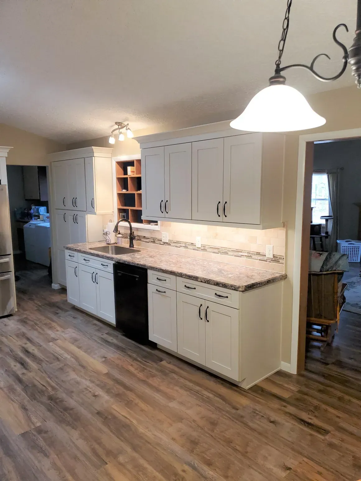 A kitchen featuring white cabinets, granite countertops, a black dishwasher, and wood-look flooring under pendant lighting.