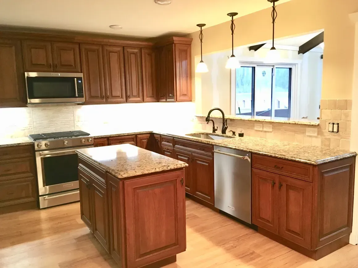 A kitchen with wooden cabinets, granite countertops, stainless steel appliances, a center island, and pendant lighting.