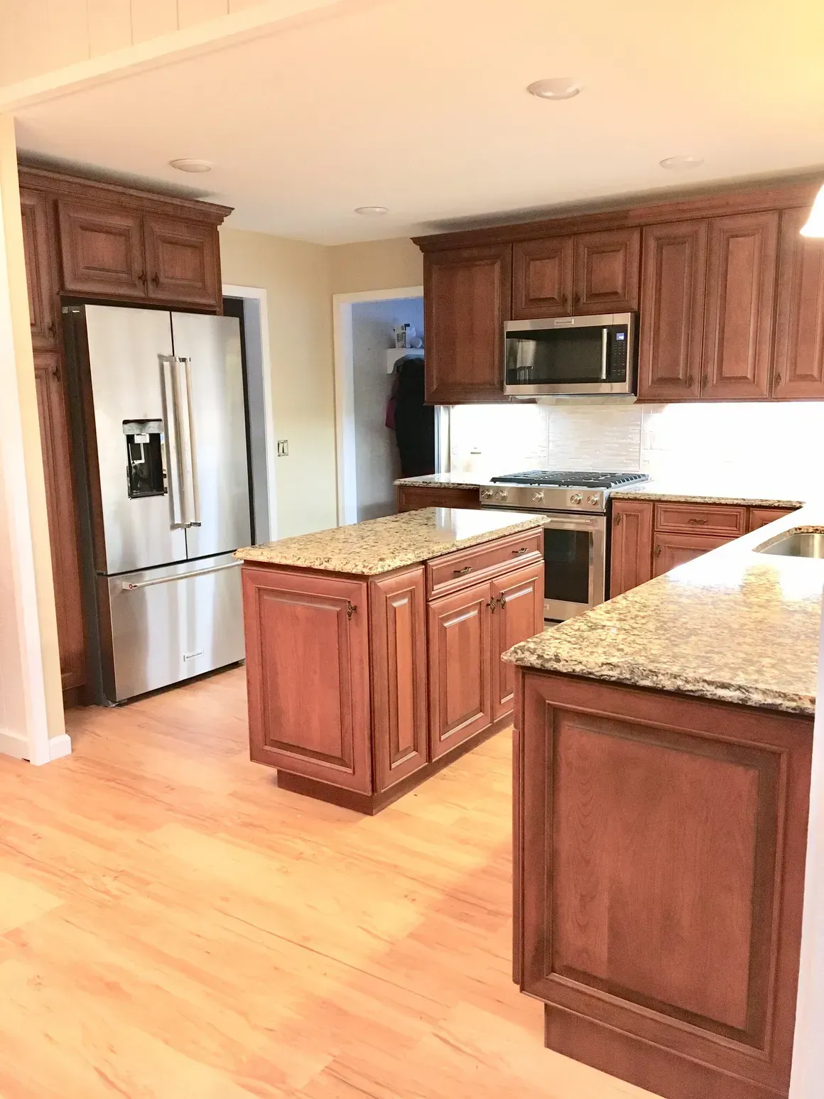 A kitchen with brown wooden cabinets, granite countertops, stainless steel appliances, and light wood flooring.