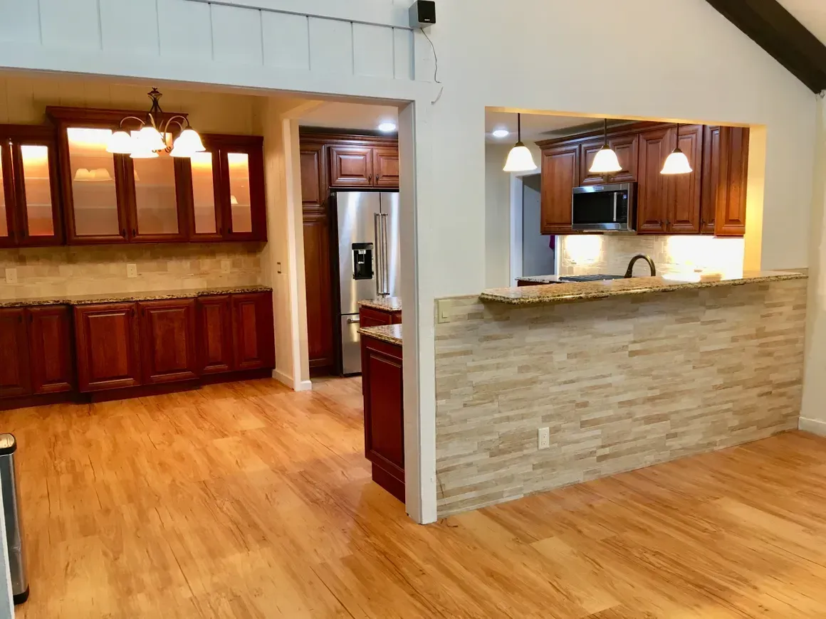 A view of a modern kitchen with wooden cabinets, light-colored flooring, and a stone-tiled breakfast bar.