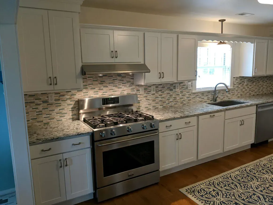 A modern kitchen featuring white cabinets, stainless steel appliances, speckled granite countertops, and a tile backsplash.