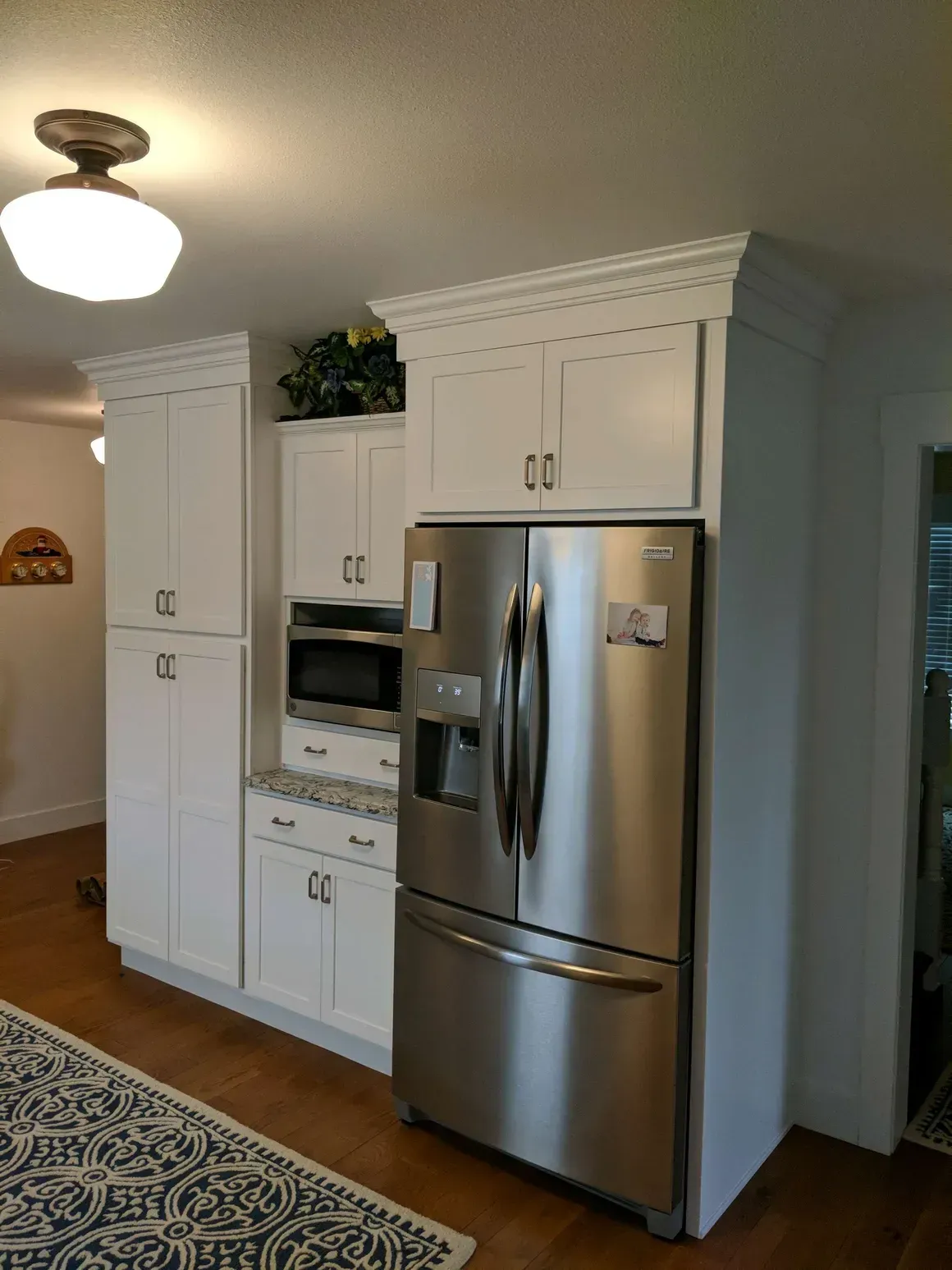 Stainless steel French-door refrigerator beside white kitchen cabinets and a built-in microwave, with patterned flooring.