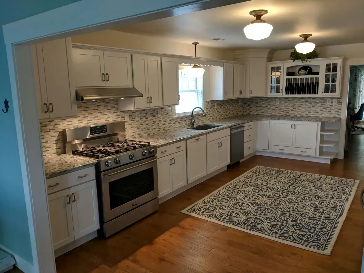 A bright kitchen with white cabinets, stainless steel appliances, speckled countertops, and a patterned area rug.