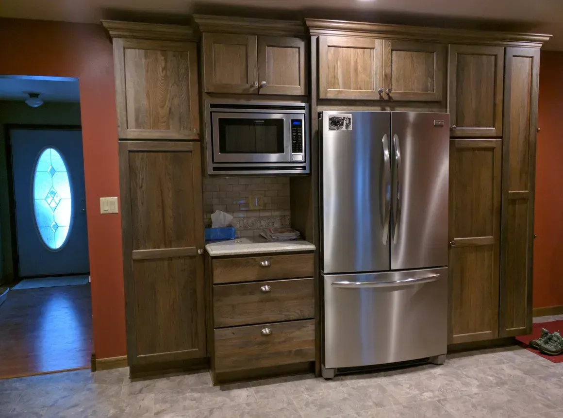 A modern kitchen wall features dark wood cabinetry, a built-in microwave, and a stainless steel refrigerator.