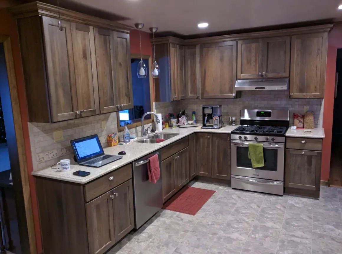 A modern L-shaped kitchen with wood cabinets, stainless steel appliances, a grey countertop, and a laptop on the counter.