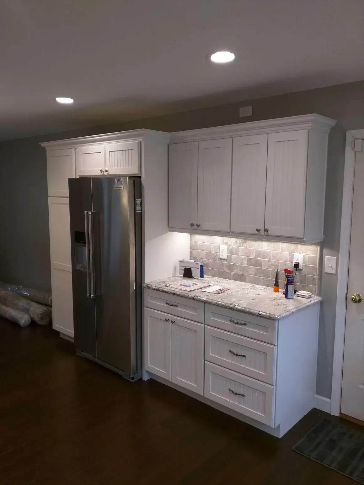 A modern kitchen featuring white cabinets, a stainless steel refrigerator, patterned tile backsplash, and stone countertops.