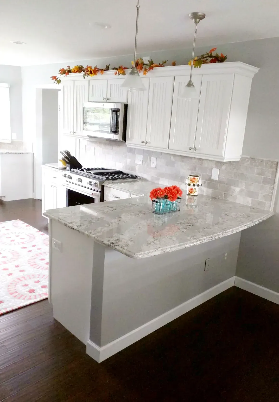 A modern kitchen featuring white cabinets, granite countertops, a stainless steel oven, and autumn-themed decor.