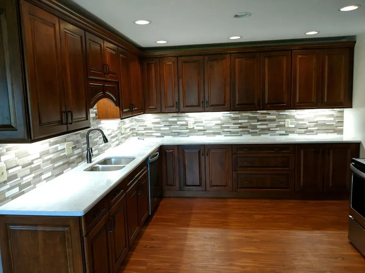 A kitchen featuring dark wood cabinets, a white countertop, and a tiled backsplash with under-cabinet lighting.