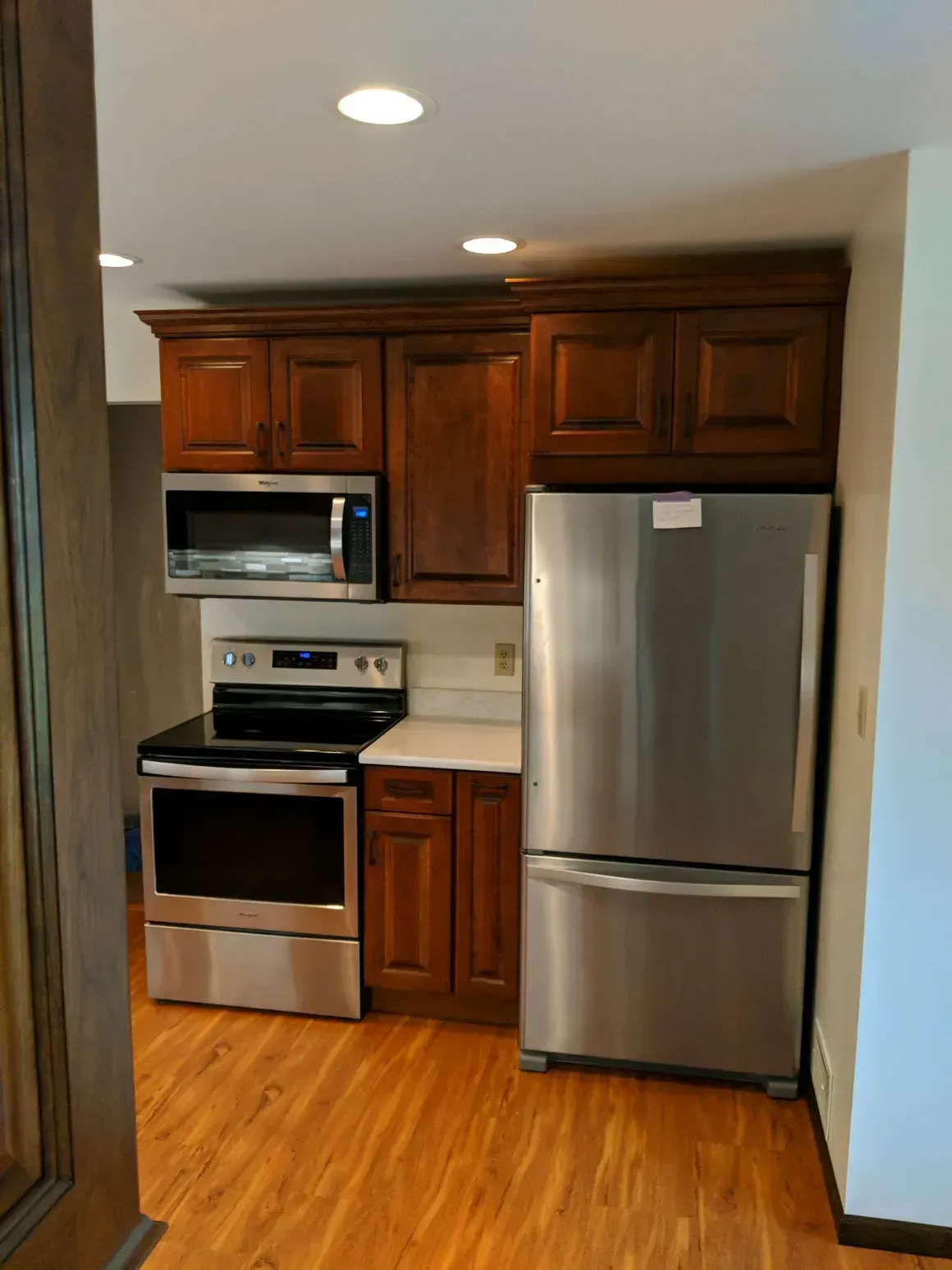 A kitchen area featuring dark wood cabinets, a stainless steel stove, microwave, and refrigerator on a wood-look floor.