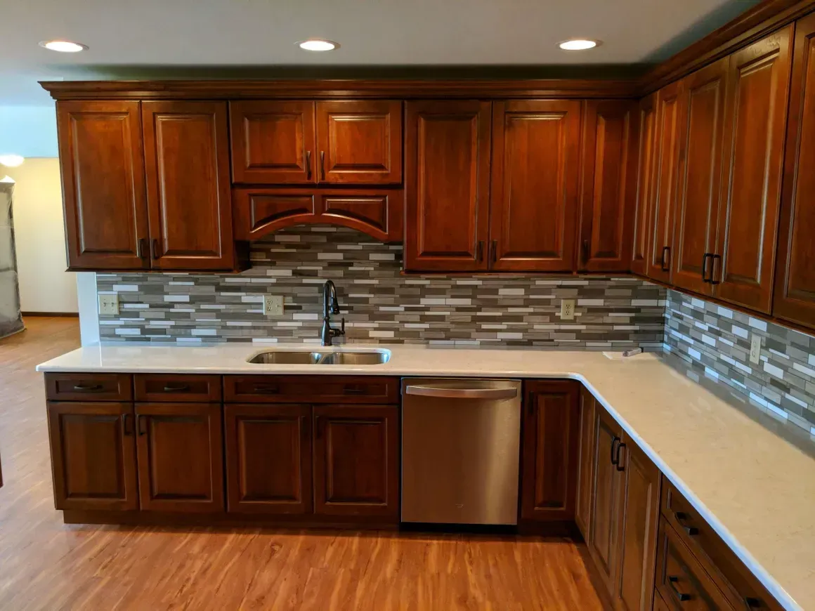 Modern kitchen with dark wood cabinets, white countertops, stainless steel dishwasher, and a grey tile backsplash.