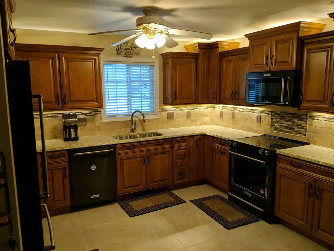 A kitchen with wooden cabinets, stone tile backsplash, light countertops, black appliances, and a central ceiling fan.