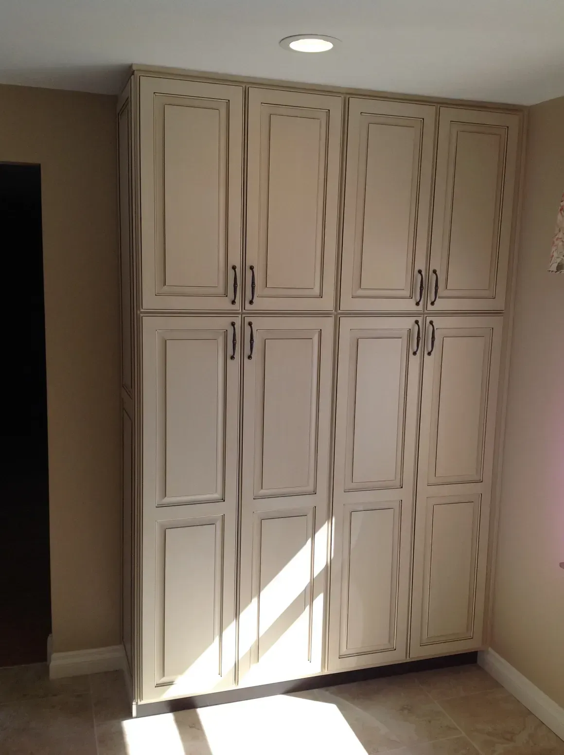 A floor-to-ceiling cream-colored storage cabinet with eight panel doors and dark hardware in a neutral-toned room.