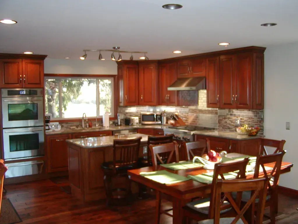 A kitchen with cherry wood cabinets, granite countertops, stainless steel appliances, and a dining table with chairs.
