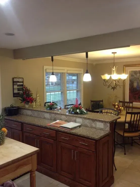 A kitchen island with brown cabinets and granite countertops, with pendant lights above and a dining area in the background.