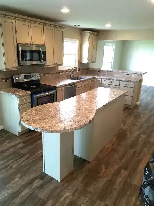 A kitchen with off-white cabinets, granite countertops, a center island with a rounded edge, and wood-look laminate flooring.