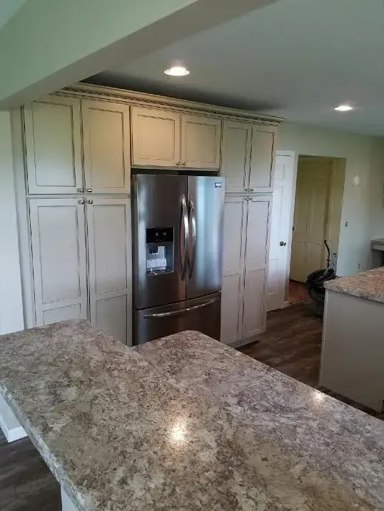 A stainless steel refrigerator is built into off-white cabinetry in a kitchen with granite countertops.
