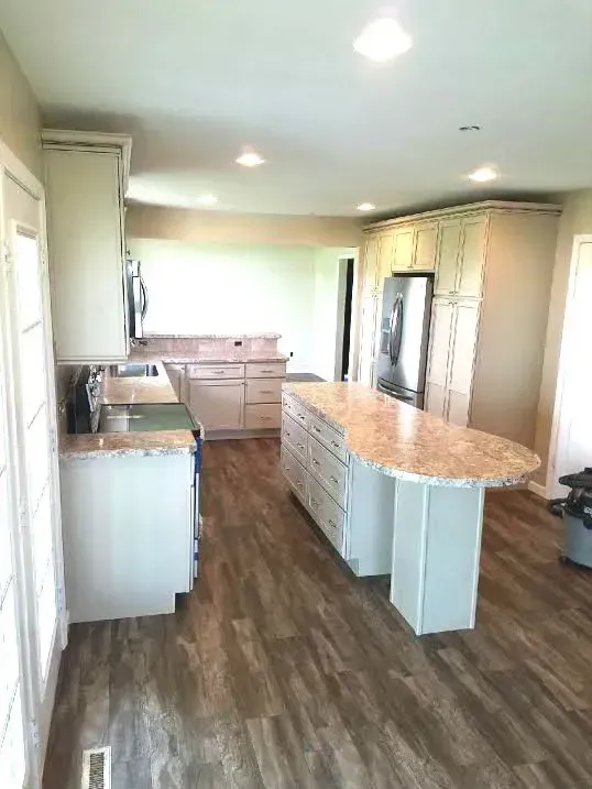 A bright, modern kitchen featuring white cabinets, a large curved granite-topped island, and light wood-plank flooring.