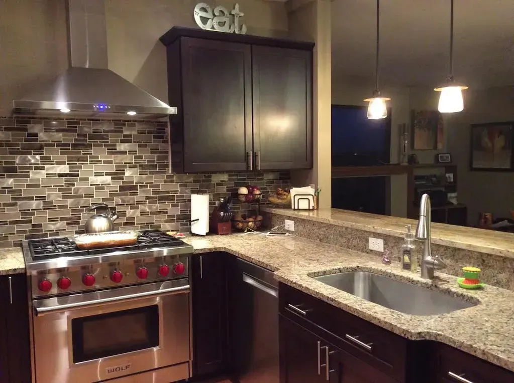 A modern kitchen with dark wood cabinets, granite countertops, a stainless steel gas stove, and a tiled backsplash.