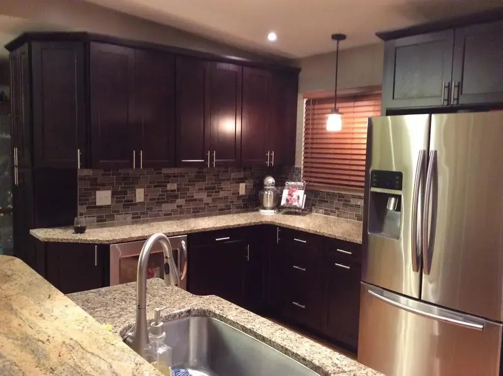 Kitchen with dark wood cabinetry, granite countertops, stainless steel appliances, and a tiled backsplash.