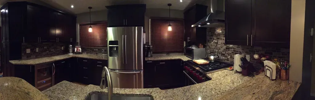 A wide-angle shot of a modern kitchen with dark wood cabinets, granite countertops, and stainless steel appliances.