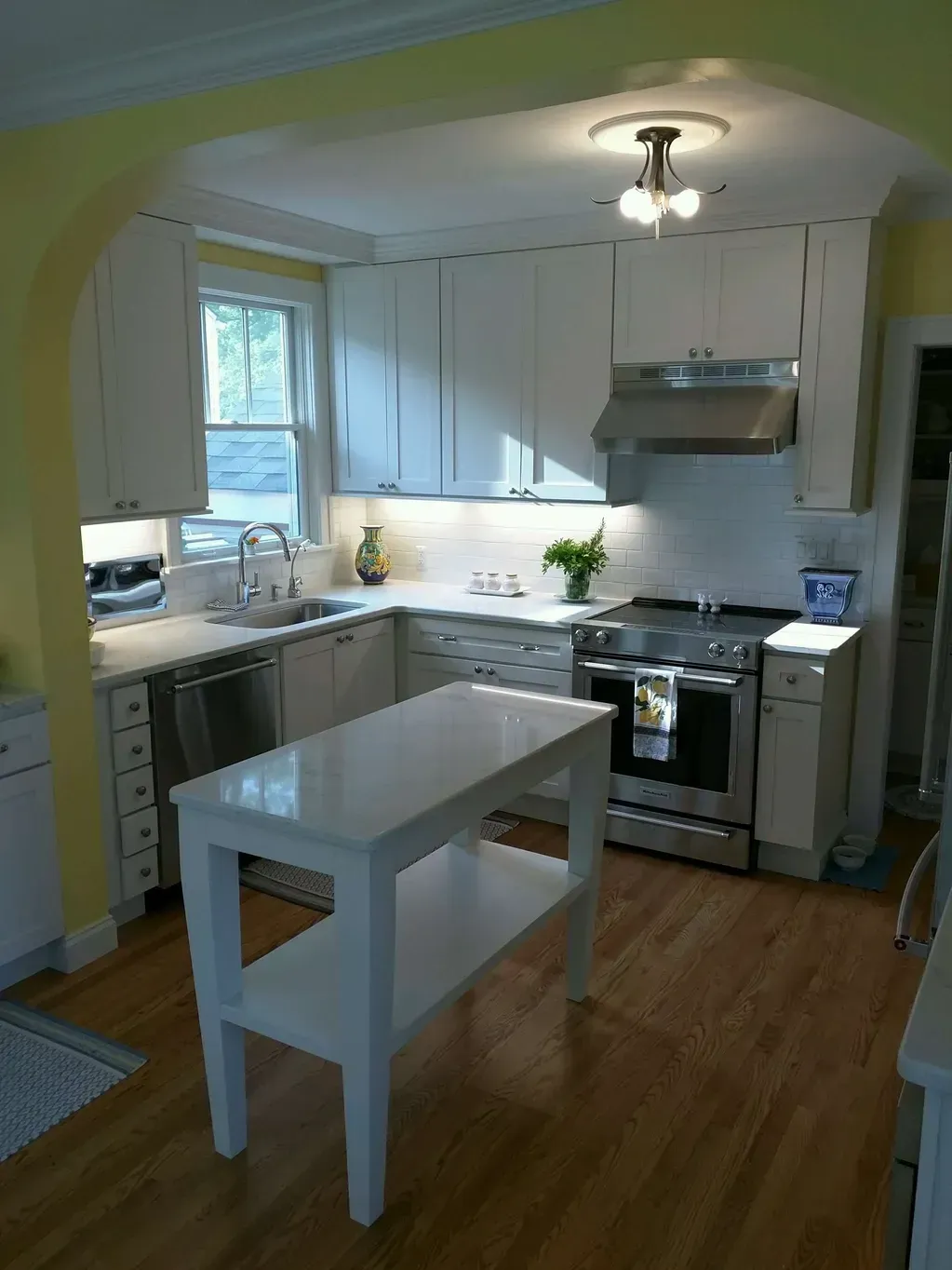 A modern kitchen featuring white cabinets, stainless steel appliances, a center island, and hardwood floors.
