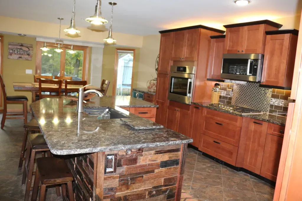 A kitchen with a stone-accented island, granite countertops, cherry wood cabinetry, and pendant lighting.