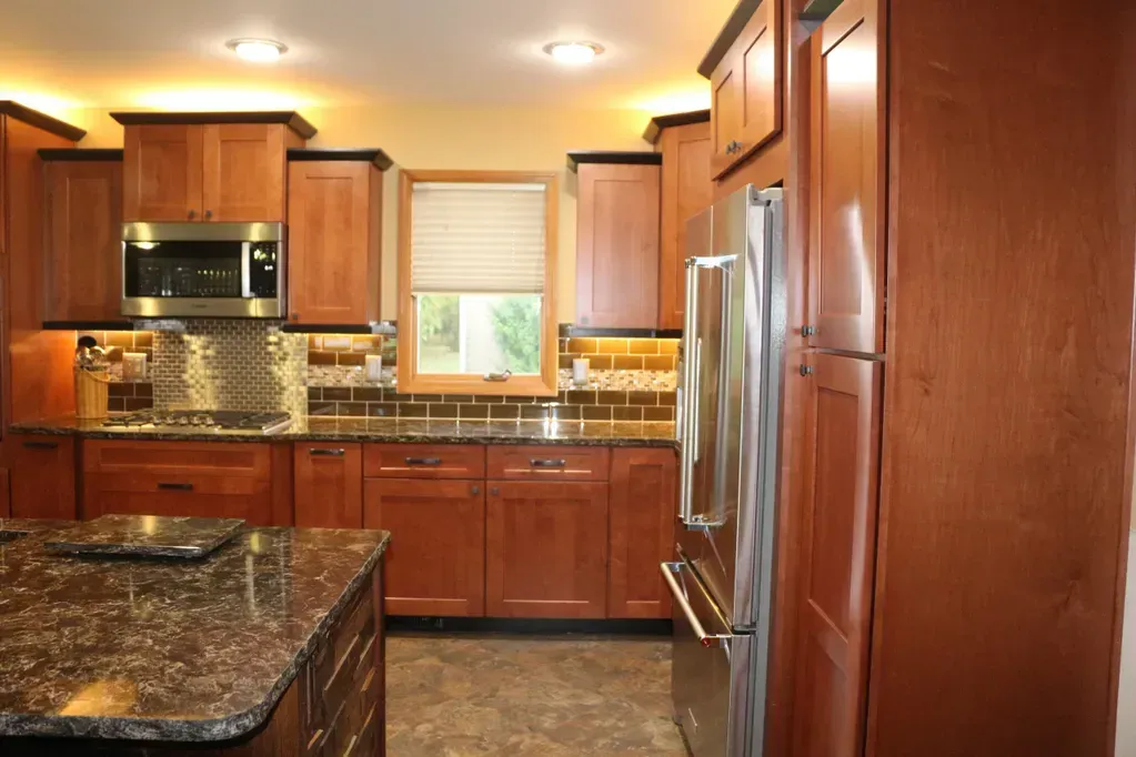 Modern kitchen with cherry wood cabinets, dark granite countertops, stainless steel appliances, and a central island.