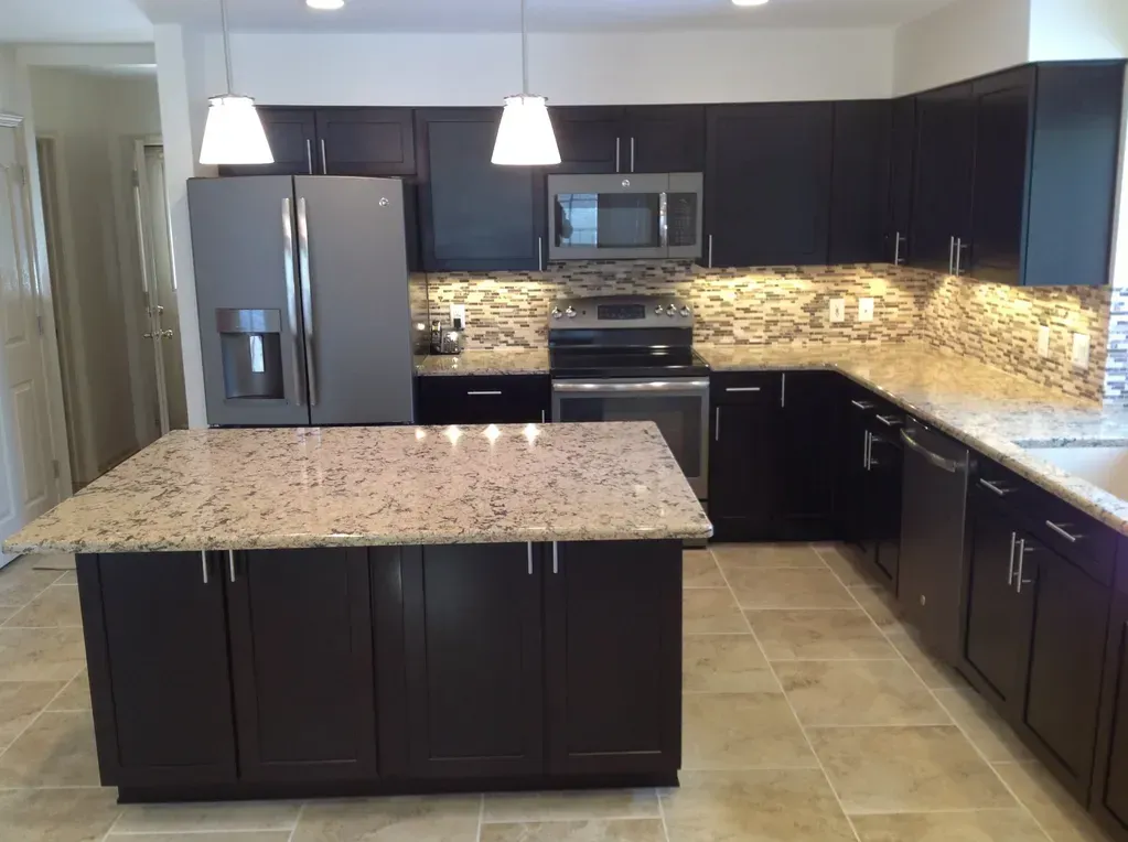 A modern kitchen with dark brown cabinets, granite countertops, stainless steel appliances, and a central island.