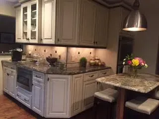 A kitchen featuring white cabinets, granite countertops, under-cabinet lighting, and a small table with two stools.