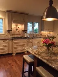 A bright kitchen with beige cabinets, a gas stove, stone countertops, a central island with stools, and wooden floors.