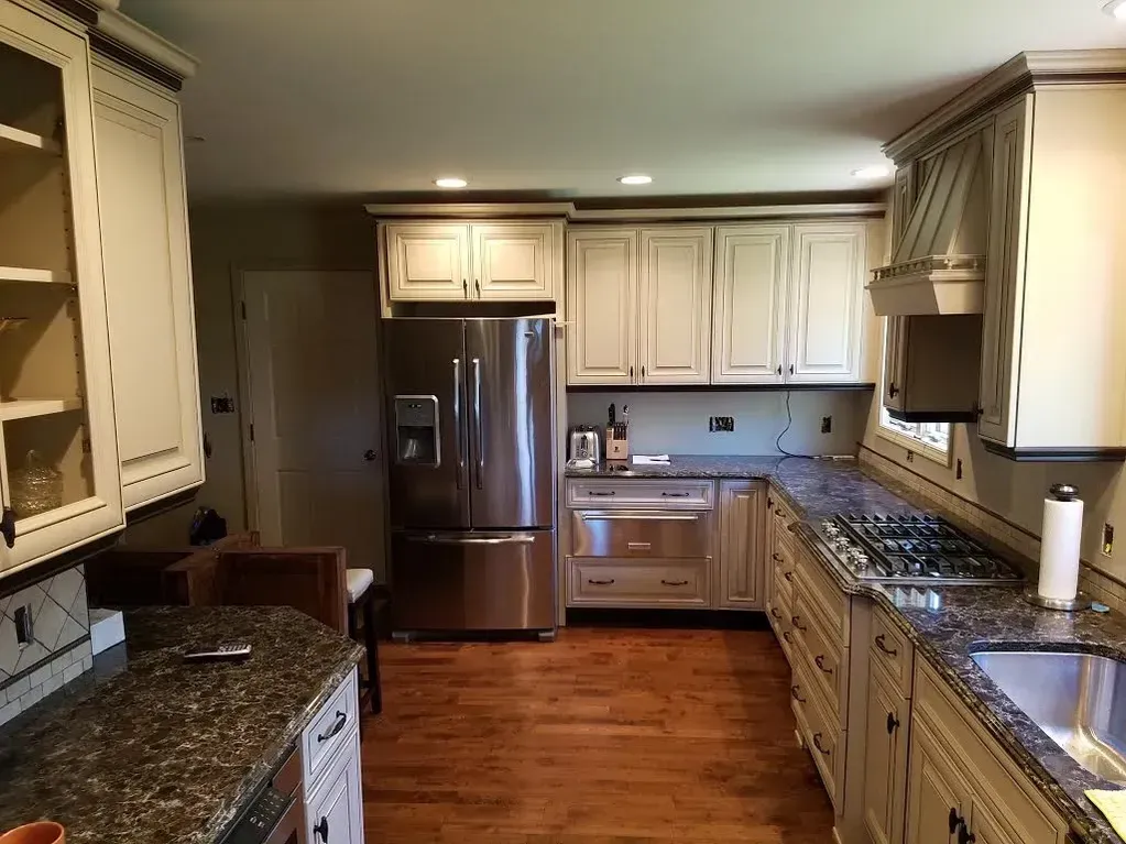 A kitchen with off-white cabinets, speckled granite countertops, stainless steel appliances, and wood flooring.