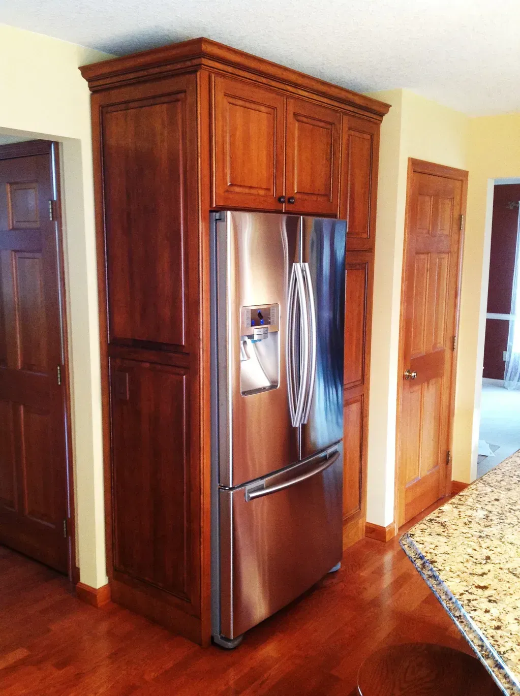 A stainless steel refrigerator built into custom wooden cabinetry in a kitchen with hardwood floors.