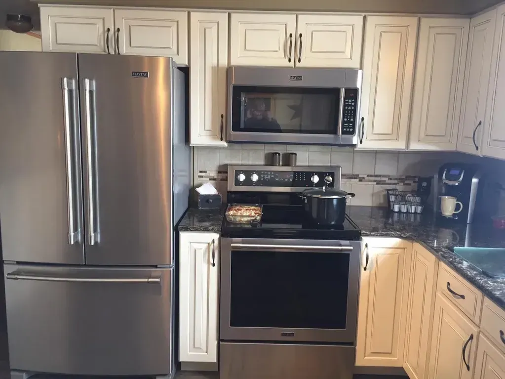 Stainless steel refrigerator, microwave, and range in a kitchen with off-white cabinets and dark granite countertops.