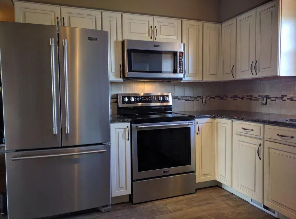 A modern kitchen featuring stainless steel appliances, white cabinetry, and a decorative tile backsplash.