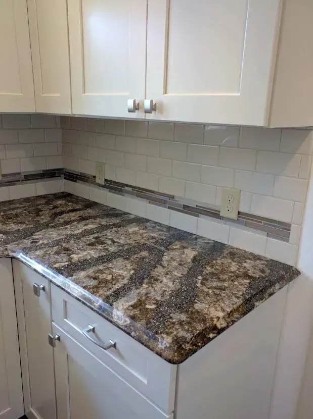 White kitchen cabinets with granite countertops and a white subway tile backsplash featuring a gray mosaic accent strip.