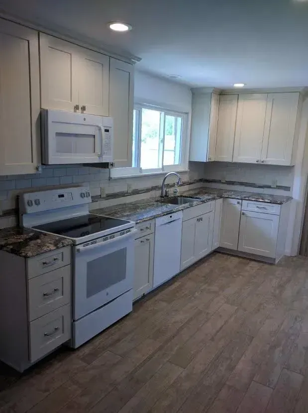 A bright kitchen featuring white cabinets, stainless steel appliances, speckled stone countertops, and wood-look flooring.