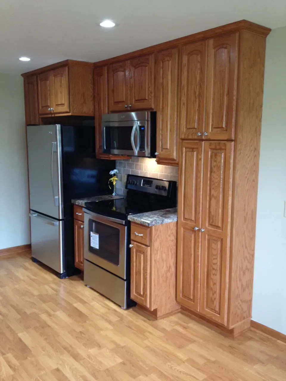 A kitchen corner with oak cabinets, stainless steel appliances, and wood flooring.