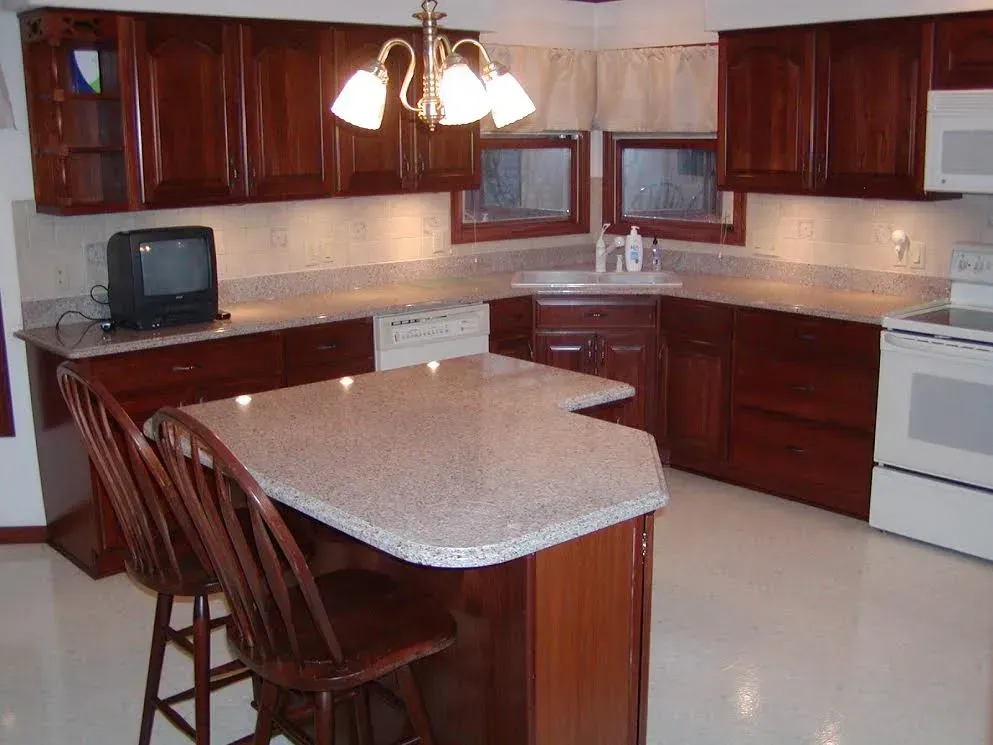 A kitchen with dark wood cabinets, light granite countertops, a center island with two chairs, and white appliances.