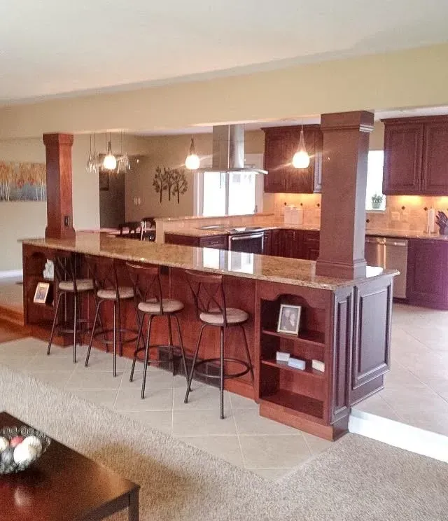 A kitchen island with four bar stools, granite countertops, and wooden cabinetry in an open-concept living space.
